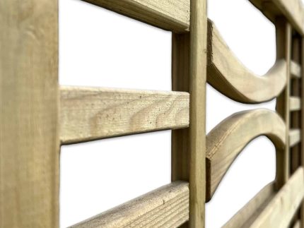 Nærbillede af en Havelåge m/espalier trykimpr. med lodrette og vandrette lameller. Hegnets tekstur og korn er tydeligt synlige, hvilket giver det et rustikt udseende. Nogle af de vandrette lameller er let buede. Baggrunden er hvid.