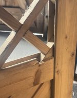 Nærbillede af en Havelåge tæt trykimpr-træstruktur med krydsende diagonale og lodrette bjælker. Sollyset fremhæver de ru kanter, træets årer og splinter, mens baggrunden er sløret.