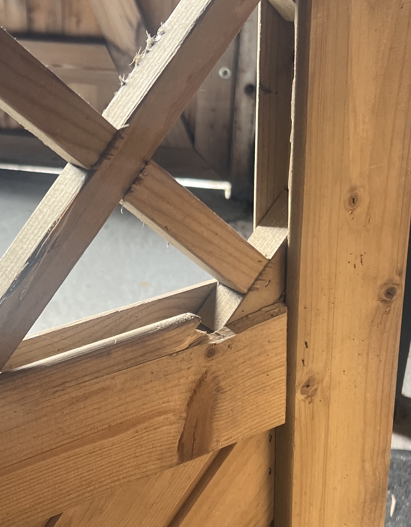 Nærbillede af en Havelåge tæt trykimpr-træstruktur med krydsende diagonale og lodrette bjælker. Sollyset fremhæver de ru kanter, træets årer og splinter, mens baggrunden er sløret.