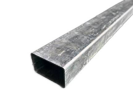 Et nærbillede af et langt, rektangulært metalrør med en firkantet hul sektion. Stålstolper 60x40mm / 2mm Varmgalvaniseret - Uden beslag ser ud til at have en galvaniseret, let ru overflade. Den er placeret diagonalt med den åbne ende vendt mod nederste venstre hjørne af billedet.