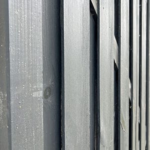 Nærbillede af et udsnit af en Havelåge Antracit 180x100cm malet i mørkegrå. Billedet fanger teksturen af de lodrette planker og træets årer. Perspektivet er let vinklet og viser dybde og kontrast mellem plankerne.