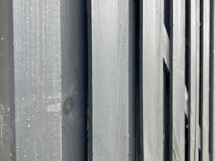 Nærbillede af et udsnit af en Havelåge Antracit 180x100cm malet i mørkegrå. Billedet fanger teksturen af de lodrette planker og træets årer. Perspektivet er let vinklet og viser dybde og kontrast mellem plankerne.