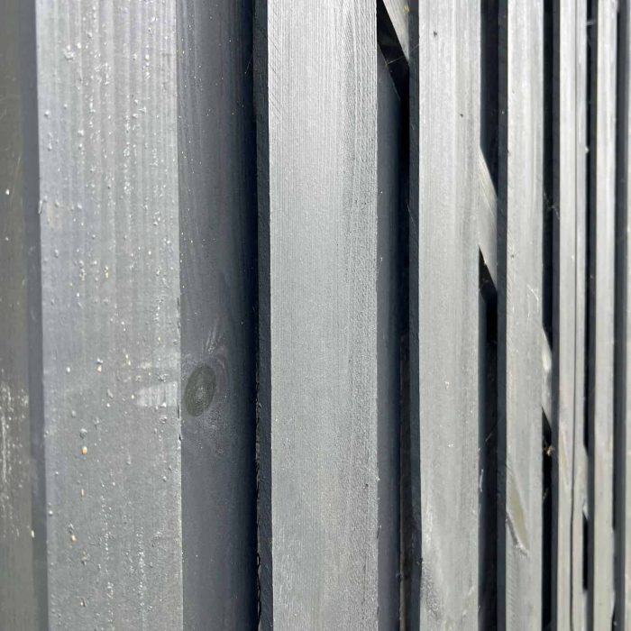 Nærbillede af et udsnit af en Havelåge Antracit 180x100cm malet i mørkegrå. Billedet fanger teksturen af de lodrette planker og træets årer. Perspektivet er let vinklet og viser dybde og kontrast mellem plankerne.