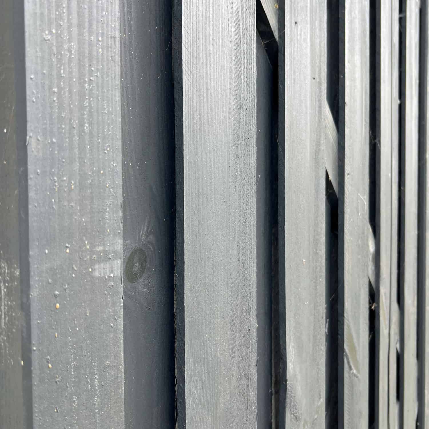 Nærbillede af et udsnit af en Havelåge Antracit 180x100cm malet i mørkegrå. Billedet fanger teksturen af de lodrette planker og træets årer. Perspektivet er let vinklet og viser dybde og kontrast mellem plankerne.