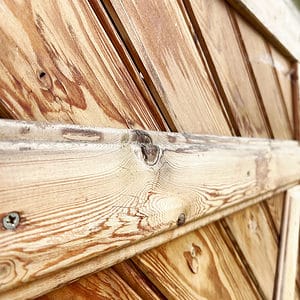 Et nærbillede af Havelåge lærketræ 100x180cm afslører dets synlige åremønstre og knaster. Træplankerne er anbragt diagonalt og holdt sammen af vandrette bjælker. Teksturen og den naturlige træfarve er fremtrædende i billedet.