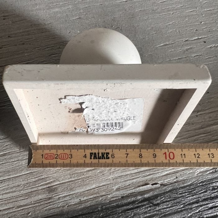 En Stolpehat m/kugle kunststof hvid, med rund top og flad bund, er vist på hovedet på træ. En lineal foran måler cirka 12 cm, og et iturevet stregkodemærke er synligt på bunden.