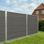 Et højt, moderne privatlivshegn lavet af Kompositbræt 25mm - WPC Træstruktur med grå paneler og metalstolper står på en trimmet græsplæne. I baggrunden ses et murstenshus og en delvis overskyet himmel.