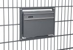 En Postkasse til indbygning i panelhegn - Antracit 7016 Mat er monteret på en sort metal panelhegn. Den rektangulære grå postkasse har et toplåg til ilægning af post og en lille slids i højre side til at hente den. Panelhegn består af lodrette og vandrette stænger, der komplementerer indbygningens slanke design.