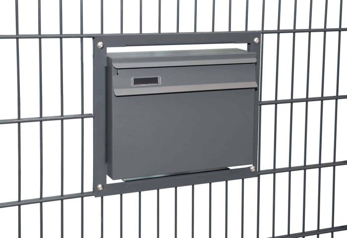 En Postkasse til indbygning i panelhegn - Antracit 7016 Mat er monteret på en sort metal panelhegn. Den rektangulære grå postkasse har et toplåg til ilægning af post og en lille slids i højre side til at hente den. Panelhegn består af lodrette og vandrette stænger, der komplementerer indbygningens slanke design.