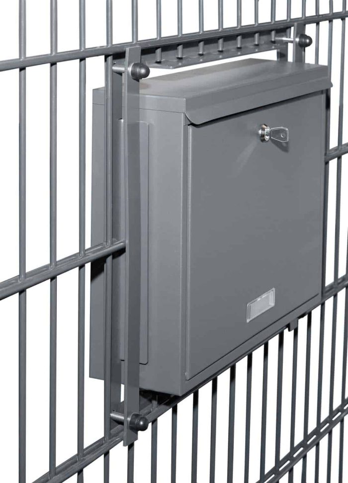 En Postkasse til indbygning i panelhegn - Antracit 7016 Måtte er monteret på et metalhegn. Den grå, aflåselige postkasse har en lille spalte til aflevering af post og et nøglehul til sikring af indholdet.