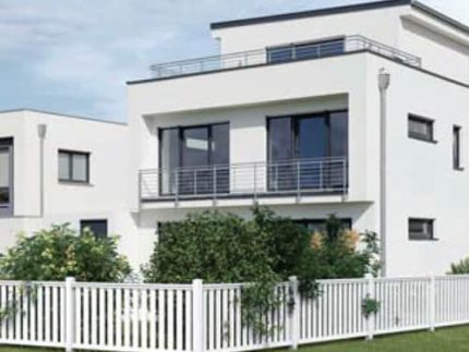 Et moderne, hvidt hus i to etager med store vinduer, en balkon med et lækkert rækværk og et fladt tag. Forhaven er omsluttet af et Hegnselement i Plast "Gelænder" 200x90cm (AVLET), suppleret med buske og grønt græs i haven. Et andet lignende hus er delvist synligt ved siden af.