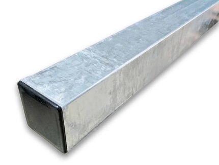 Et nærbillede af Stålstolper Galvaniseret 80x80cm HDG Inkl. sort stolpehat i plast med en struktureret, skinnende overflade. Den ene ende af røret er lukket med et mørkt, firkantet plaststykke. Røret er placeret diagonalt og strækker sig fra nederste venstre hjørne til øverste højre hjørne af billedet.