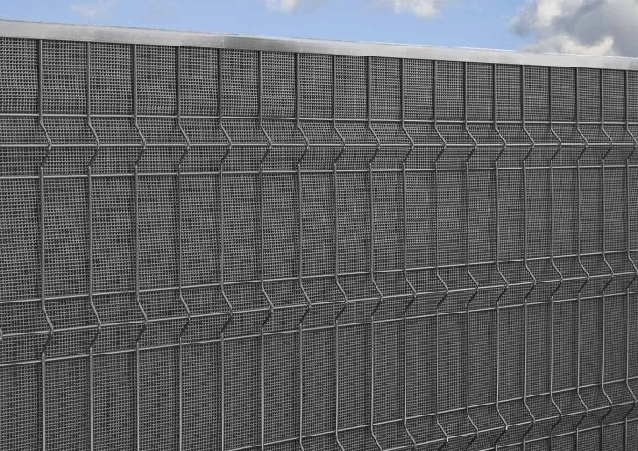 Et nærbillede af Støjhegn ECO 18Db Modul med grå metalnetfacade i zigzag mønster. Designet skaber gentagne geometriske former med skygger, hvilket giver et struktureret og struktureret udseende. Himlen er delvist synlig med nogle skyer i baggrunden.
