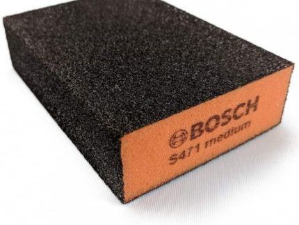 En rektangulær Vaskbar slibesvamp til komposithegn med en orange side og en sort slibende side. Den orange side har BOSCH-logoet og teksten "S471 medium." Denne alsidige slibesvamp er perfekt til at slibe overflader omkring dit hjem eller endda forberede dit komposithegn til et frisk lag maling.