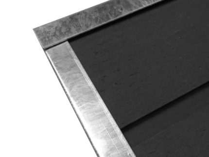 Et nærbillede af U-skinne top/bund - varmgalvaniseret, en rektangulær, metallisk genstand med sort overflade. Topskinne-rammen rundt om kanterne skaber et rent, moderne look. Objektets øverste venstre hjørne er i fokus og fremhæver materialernes tekstur og glans.