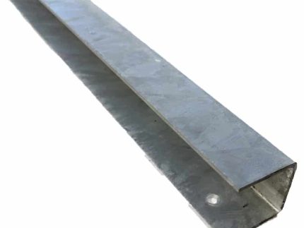 Et nærbillede af et langt metalvinkeljern med galvaniseret finish. Denne L-formede U-skinne top/bund - varmgalvaniseret har en 90 graders bøjning. Der er forborede huller langs den ene side nær kanten, og overfladen har en lidt ru tekstur.