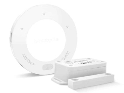 En hvid, rund smart home-enhed med indikatorlys og logo på fronten er placeret ved siden af en mindre rektangulær sensor og en flad magnetstrimmel. Dette er ismartgate LITE - Fjernstyret Låge & portåbner via. Din Smartphone eller PC (Max 1 tilslutning af låge eller port), perfekt til dem, der har brug for en fjernstyret portløsning. Objekterne er placeret på en hvid baggrund.