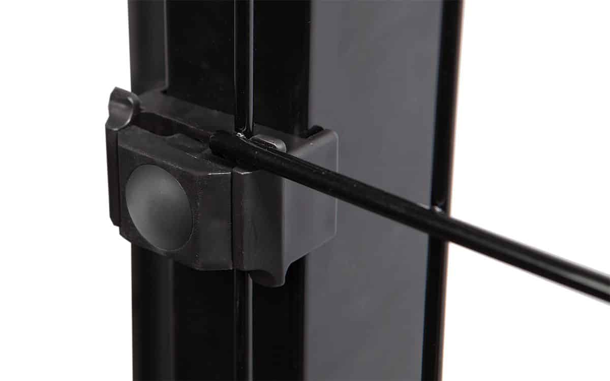 Et nærbillede viser en del af en metallisk sort ramme med en klemme, der fastgør en tynd sort stang til den. Klemmen, der ligner Punkt Beslag Sæt til 60x40 stolper/panelhegn, har en knap eller knop på siden. Billedet fokuserer på forbindelsespunktet og fremhæver fastgørelsesmekanismen.