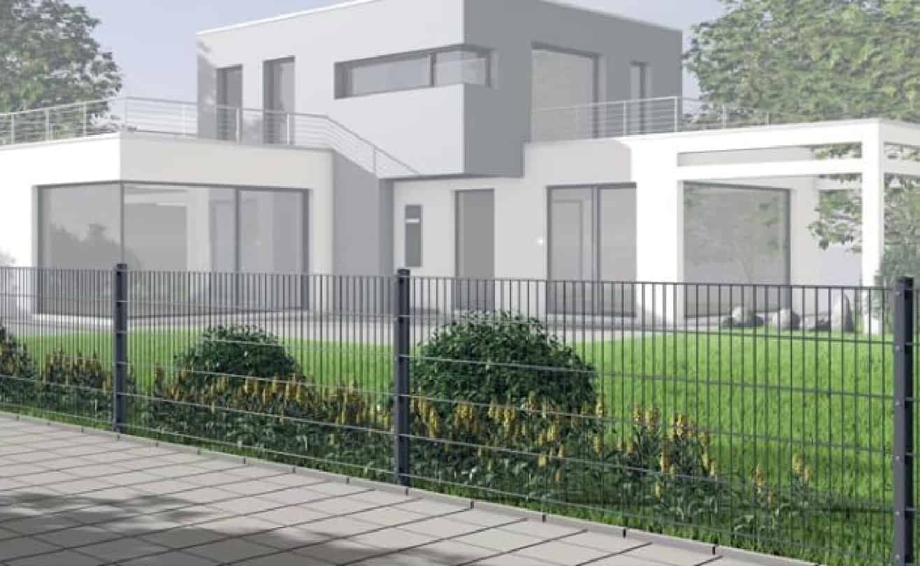 Moderne to-etagers hus med store vinduer og balkon, med hvidt og gråt ydre. Boligen ligger bag en sort metalhegn, der giver beskyttelse til en stor, pænt anlagt grøn græsplæne og buske. Forgrunden viser en flisebelagt gangbro foran hegnet.