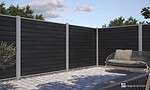 Et moderne udendørs terrasseområde med slankt sort vandret lamelhegn lavet af Komposit Hegn med galvaniseret stålstolper & u-skinner - Type 1 og grå støttestolper. Terrassen har en potteplante til venstre og en polstret sofa med en taupe-pude til højre, alt sammen sat på lysegrå stenbelagt jord. Himlen er delvist overskyet.