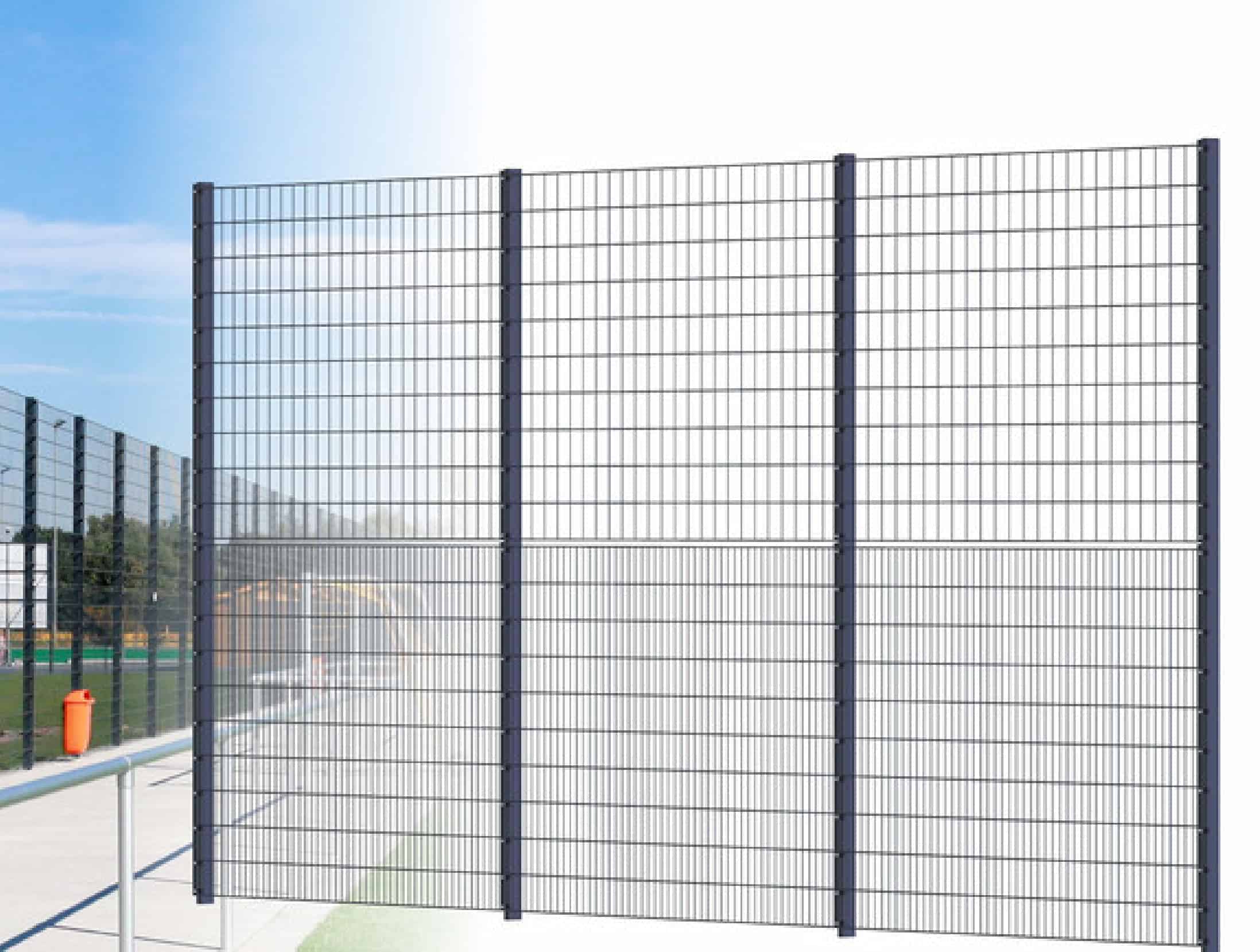 Billedet viser et højt, sort metaltrådhegn med flere lodrette og vandrette stænger, hvilket skaber et gitterlignende udseende. Dette panel hegn "BALLSTOP" 2D SPORT er installeret udendørs, med blå himmel og en del af et 2D SPORT-felt synligt i baggrunden.