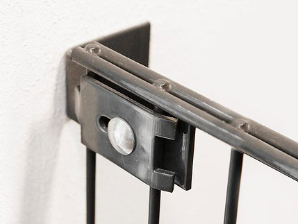 Nærbillede af et sort metalgelænder, der er fastgjort til en hvid væg med et rektangulært Væg/vinkel Beslag, sikret med en stor rund bolt.
