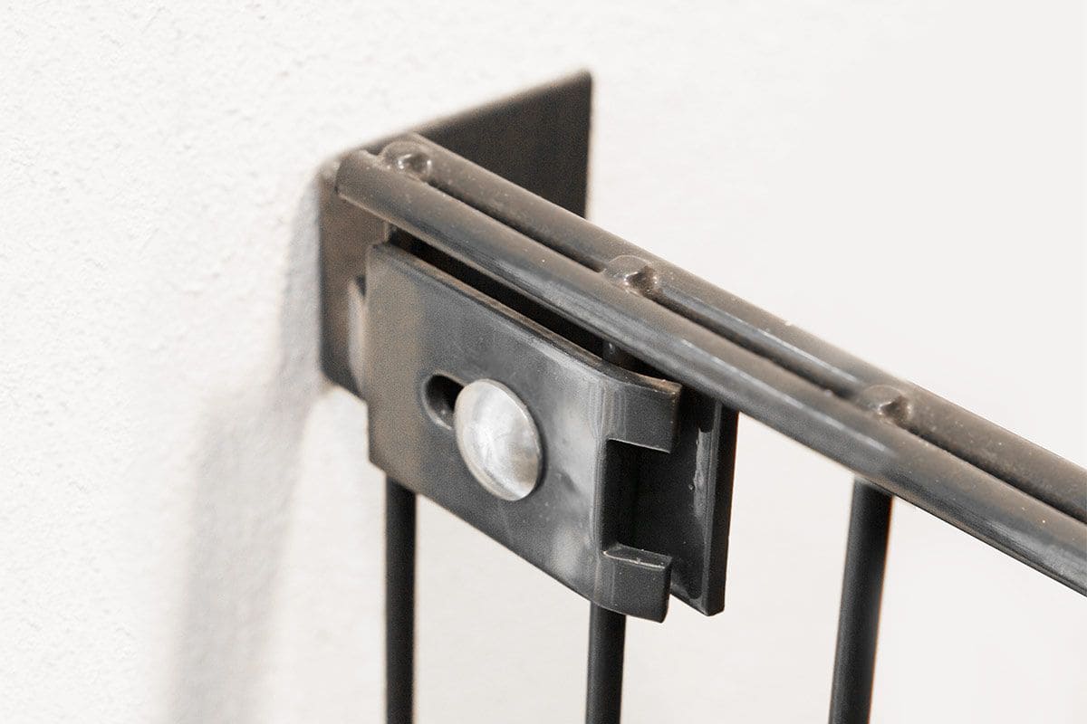 Nærbillede af et sort metalgelænder, der er fastgjort til en hvid væg med et rektangulært Væg/vinkel Beslag, sikret med en stor rund bolt.