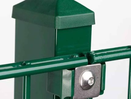 Nærbillede af en grøn metal hegnspæl med en hætte og en vandret stang fastgjort ved hjælp af en Holdeplade med hul - Rustfrit stål beslag og bolt. Baggrunden er almindelig hvid, hvilket fremhæver posten og dens forbindelseskomponenter.