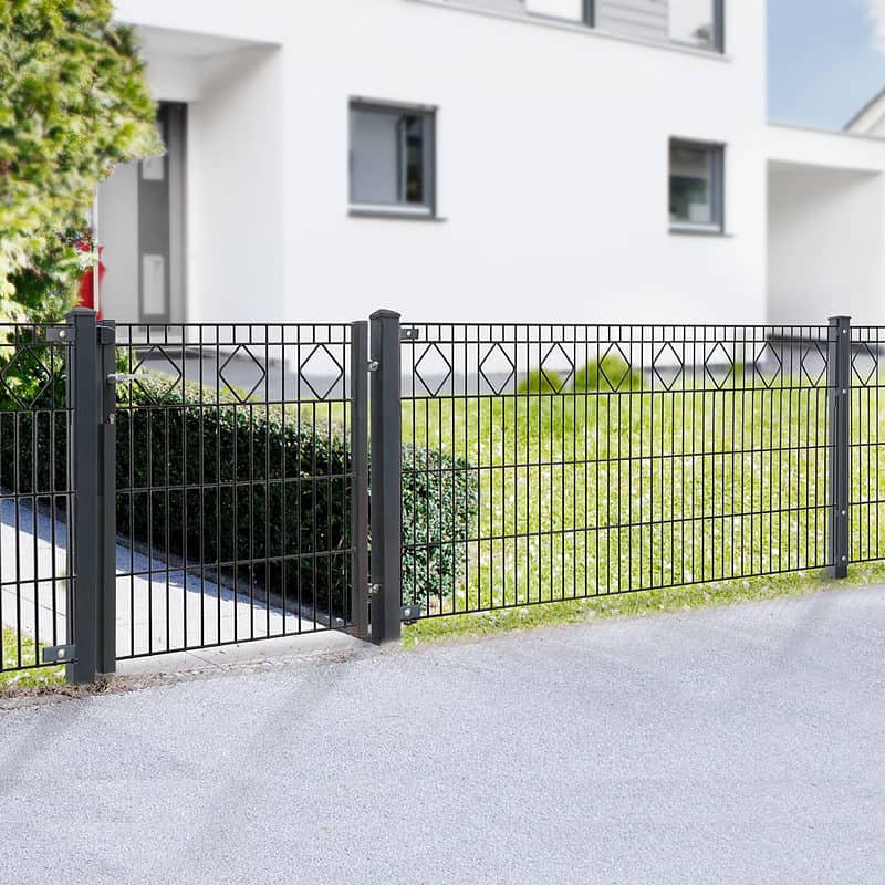 Et moderne hegn, Panelhegn med mønster Pulverlakeret Sort Metal Inkl. Stålstolper & Beslag, har lodrette stænger og et diamantformet design nær toppen. Placeret foran et hvidt, moderne hus med flere vinduer, komplementerer det den velholdte græsplæne og grønne områder, der er synlige bag hegnet.