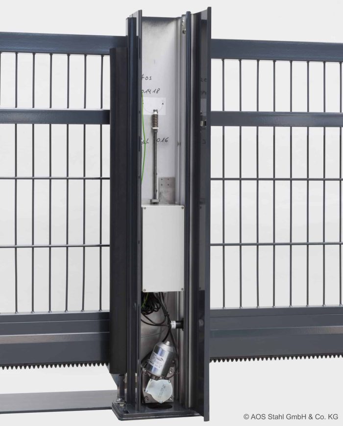 Et nærbillede af en automatisk portsystemkomponent, der viser den indvendige mekanisme anbragt i et lodret metalhus. Huset, integreret i et Skydeport "V-Star EXTREME" 2D Panelfyldt 8/6/8 MM metalhegn med lodrette og vandrette stænger, afslører den indviklede mekanisme inklusive ledninger og en motorkomponent.