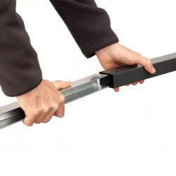 En person iført en mørk langærmet skjorte demonstrerer Stolpeforstærkning 60x40mm / 120cm Galvaniseret ved at samle to metalbjælker, hvorved en sort rektangulær bjælke skydes over en sølvfarvet. Baggrunden er almindelig hvid.