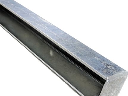 Et nærbillede af U-skinne side - Varmgalvaniseret, en lang, metallisk rektangulær stang med en smal sort strimmel, der løber langs dens længde, placeret mod en almindelig hvid baggrund. Den varmgalvaniserede stang har en skinnende, reflekterende overflade og fremstår robust og industriel.