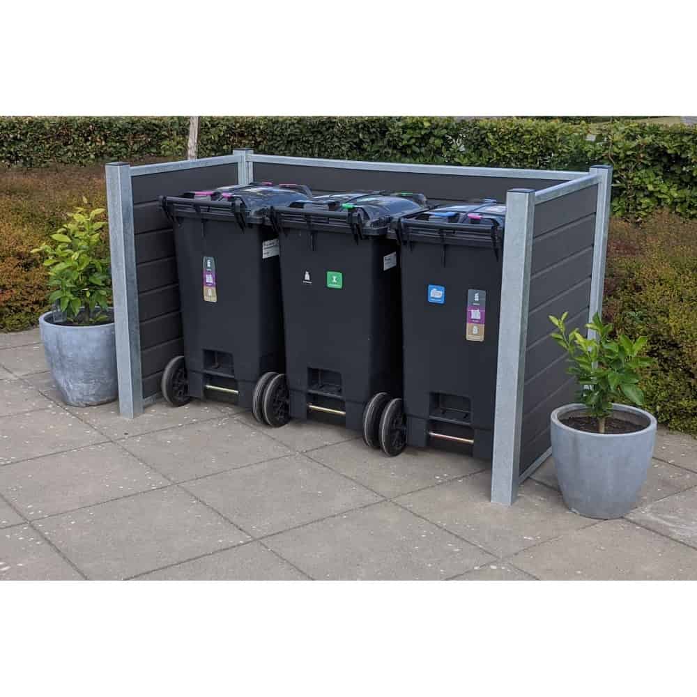 Tre sorte skraldespande med forskellige farvede låg er placeret side om side i en Komposit skraldespandsskjul understøttet af stålstolper. Området er flisebelagt med lys grå beton, og to store grå krukker med små grønne planter flankerer børstets sorteringsspande.