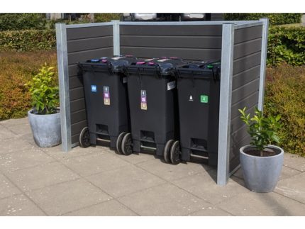 Et sæt med tre sorte skraldespande placeret i en skraldespandsskjul med stålstolper udendørs. Hver beholder har forskellige farvede låg og etiketter til genbrugskategorier. På hver side af børstet sorteringsspande står store potteplanter. Området er belagt med grå fliser og omgivet af grønt.