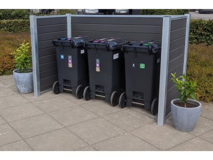 Tre sorte skraldespande er opstillet i en pæn Komposit skraldespandsskjul med grå panelvægge understøttet af stålstolper. Hver beholder har en forskellig farvet etiket, der angiver genbrug, almindeligt affald og organisk affald. To potteplanter er placeret på hver side af indhegningen, og buske er i baggrunden.