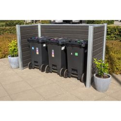 En række af tre sorte skraldespande på hjul er placeret på en asfalteret overflade. Hver beholder har forskellige farvede låg og etiketter til at sortere affald. Komposit skraldespandsskjul indhegningen, forstærket med stålstolper, inkluderer to potteplanter på hver side. Buske er i baggrunden.