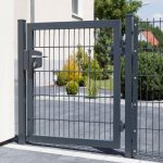 En moderne grå 2D Panellåge "TREND" galvaniseret og pulverlakeret port med lodrette og vandrette sprosser er en del af et hegn i et boligområde. Lågen er lukket og sikret med en lås. Bag porten er der anlagt landskab med grønne buske og små træer. En asfalteret gangbro er foran.