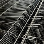 Et nærbillede af det stablede 3D panel metaltrådsnet fra Metal Hegn 3D Panel "HF-BUDGET SERIES" Inkl. Stålstolper & Fittings - Pulverlakeret Sort. Det sorte net har ensartede, parallelle tråde med rektangulære mellemrum imellem, og deres overlappende lag skaber et komplekst, geometrisk mønster med refleksioner på stålet.