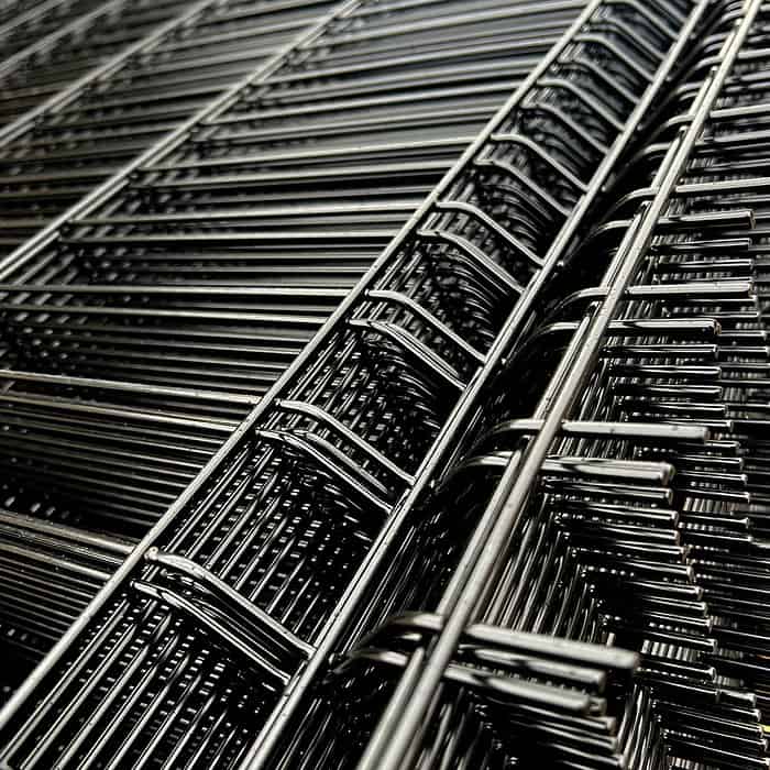 Et nærbillede af det stablede 3D panel metaltrådsnet fra Metal Hegn 3D Panel "HF-BUDGET SERIES" Inkl. Stålstolper & Fittings - Pulverlakeret Sort. Det sorte net har ensartede, parallelle tråde med rektangulære mellemrum imellem, og deres overlappende lag skaber et komplekst, geometrisk mønster med refleksioner på stålet.