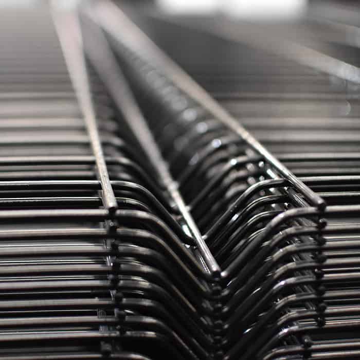 Nærbillede af en række Panelhegn 3D 5/5mm - HF PREMIUM Pulverlakeret Sort RAL 9005 trådstativer stablet sammen. Fokus er på de indviklede, gentagne linjer dannet af ledningerne, hvilket giver en følelse af dybde og strukturelt mønster. Baggrunden er sløret, hvilket fremhæver detaljerne i trådkonstruktionen.