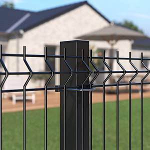 Nærbillede af et Metal Hegn 3D Panel "HF-BUDGET SERIES" Inkl. Stålstolper & Beslag - Pulverlakeret Sorter hegnspæl og trådnet hegn foran hus med terrasse. Det hvide hus har store vinduer, mens baggrunden afslører havemøbler og et delvist skyggefuldt område, hvilket tyder på en solskinsdag.