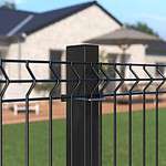 Detaljeret visning af et Metal Hegn 3D Panel "HF-BUDGET SERIES" Inkl. Stålstolper & Fittings i Pulverlakeret Sort, med et geometrisk design, med en velholdt græsplæne i forgrunden og et moderne et-plans hus med et stort dæk og udendørsmøbler i baggrunden. Den klare himmel indikerer, at det er en solskinsdag.