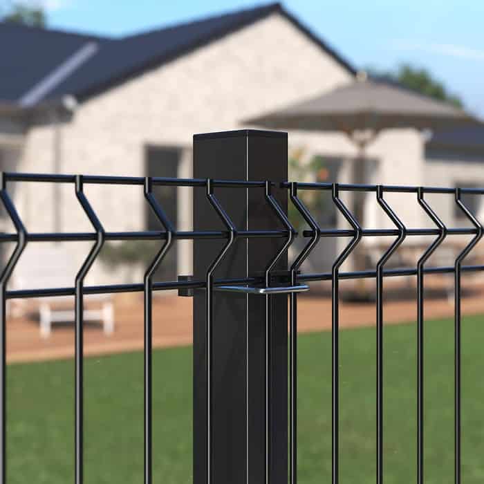 Detaljeret visning af et Metal Hegn 3D Panel "HF-BUDGET SERIES" Inkl. Stålstolper & Fittings i Pulverlakeret Sort, med et geometrisk design, med en velholdt græsplæne i forgrunden og et moderne et-plans hus med et stort dæk og udendørsmøbler i baggrunden. Den klare himmel indikerer, at det er en solskinsdag.