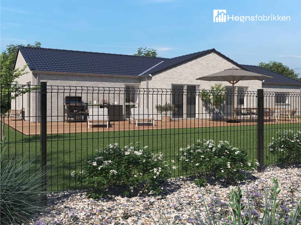 Et et-etagers hus med et mørkeblåt tegltag, lyse ydervægge og et rummeligt træterrasse. Gården er omsluttet af et sort Panelhegn 3D 4/4mm - Pulverlakeret Metal RAL 9005 Sort hegn, med et haveområde med grønne planter og hvide blomster i forgrunden.