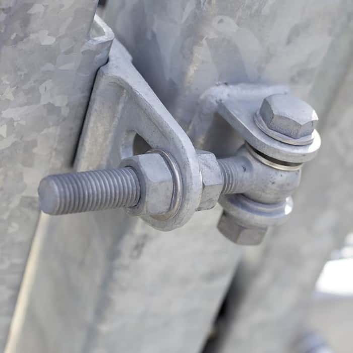 Et nærbillede viser en metalbolt og -møtrik, der sikrer to stykker 2D Panellåge "TREND" Galvaniseret/Pulverlakeret. Bolten passerer gennem en klemme, med møtrikken spændt på den, og holder sektionerne fast sammen. Den teksturerede metaloverflade antyder dens anvendelse i byggeri eller hegn, især i 2D panelportinstallationer.