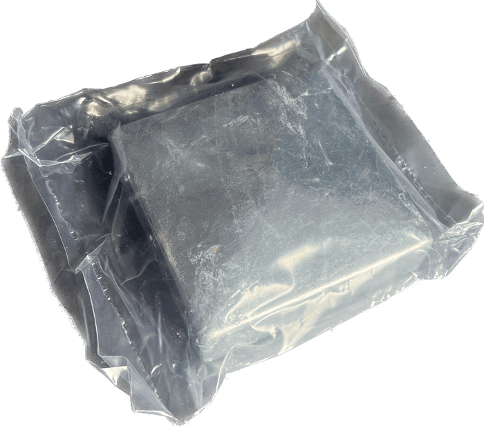 En firkantet, mørkegrå genstand lavet af Stolpehat Varm galvaniseret stål HDG 80x80mm er forseglet i en gennemsigtig plastvakuumemballagepose. Emballagen fremstår tæt og sikker og viser nogle reflekser og små krøller på plastoverfladen. Objektet indeni ser solidt og uigennemsigtigt ud.