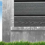 Et nærbillede af den nederste del af en bygning med mørkegrå vandret sidespor. Fundamentet ser ud til at være udført i forvitret Bundplade Galvaniseret Stål - 1815x175x35/2mm. Grønt græs er synligt ved bunden, med en blå himmel i baggrunden.