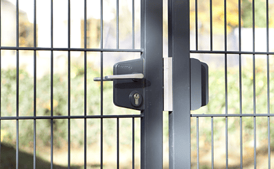 Et nærbillede af den moderne sorte Dobbeltlåge "TREND"-port, sammensat af slanke lodrette og vandrette metalstænger med en sikker Locinox låsekasse-mekanisme. Baggrunden er let sløret og viser grønt og et hegn - et perfekt eksempel på moderne design.