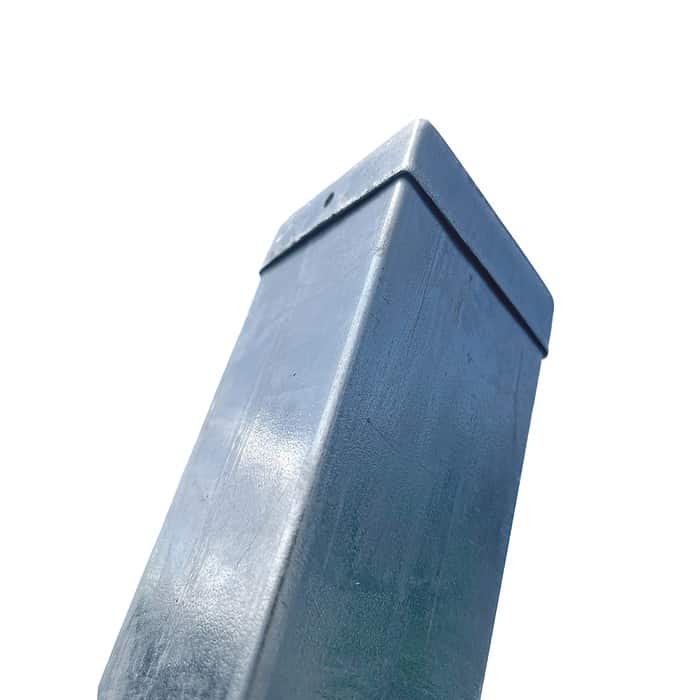 Et nærbillede af en høj, rektangulær metalstolpe med en flad tophætte, set fra en lav vinkel mod en almindelig hvid baggrund. Overfladen på Stolpehat Varm galvaniseret stål HDG 80x80mm fremstår let ridset og forvitret.