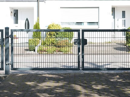 A Dobbeltlåge "TREND" komplet med Locinox låsekasse står lukket foran en bolig med hvide vægge, vinduer og buske i baggrunden.